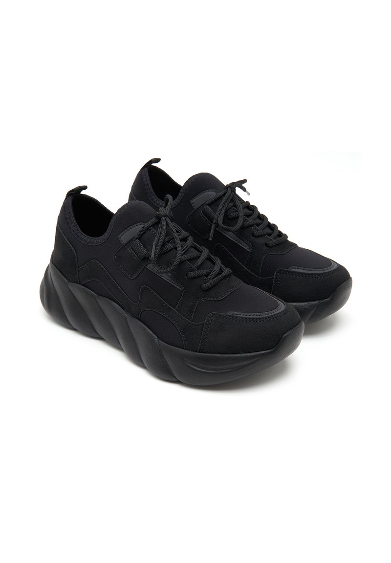 Schwarze Turnschuhe mit einem strukturierten Stoff und glatten Akzenten, ausgestattet mit einer klobigen Sohle mit wellenförmigem Design und einem standardmäßigen Schnürsystem.