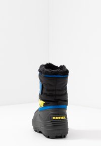 Schwarze isolierte Stiefel mit strukturierter Oberfläche, blauen Akzenten und einem gelben Logo. Sie verfügen über einen Kunstfellkragen und ein robustes Sohlen-Design.