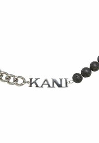 Sølv kæde med navnet "KANI" og sorte lavastenperler, der viser en kombination af metalliske og teksturerede elementer.