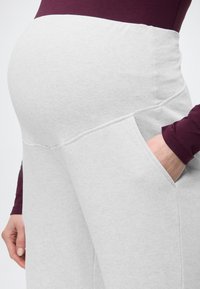 Ανοιχτό γκρι παντελόνι εγκυμοσύνης με ελαστική μέση, πλαϊνές τσέπες και απαλή υφή, σε συνδυασμό με μπορντό μακρυμάνικη μπλούζα.