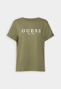 Camiseta de manga corta color verde oliva, hecha de una tela suave, con el logo blanco "GUESS" y el texto "EST. 1981" en la parte frontal. Cuello redondo.