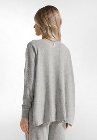 Maglione a maglia grigio chiaro con una vestibilità comoda, caratterizzato da maniche lunghe a sbuffo, polsini a costina e un piccolo etichetta sul retro del collo. Texture morbida.