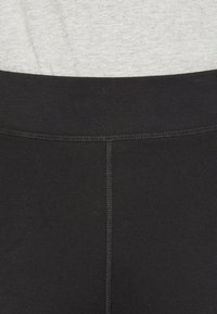 Svarta leggings med en slät yta, som har ett elastiskt midjeband och en synlig söm ner längs mitten. Tillverkade av stretchigt tyg.