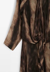 Robe à motifs marron et noir avec un drapé ample, des manches longues et une taille nouée. Le tissu texturé imite la peau de serpent.