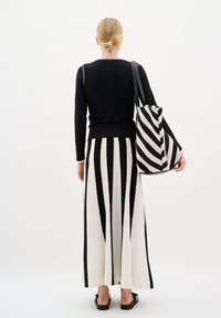 Melnas garās piedurkņu blūzes kombinācija ar baltu svārku, kuram ir vertikālas melnas svītras, turētājs ar svītrainu somu un melni sandales.