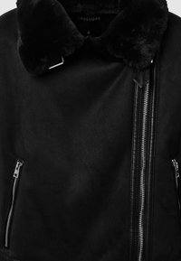 Schwarze Jacke mit Kunstfellkragen, matter Oberfläche, asymmetrischem Reißverschluss und silbernen Hardware-Details. Glatte Textur mit detaillierter Stichverarbeitung.