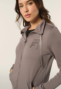 Felpa grigia con zip e colletto alto, dotata di un logo "FREDY" in strass, tasche laterali e una trama liscia.