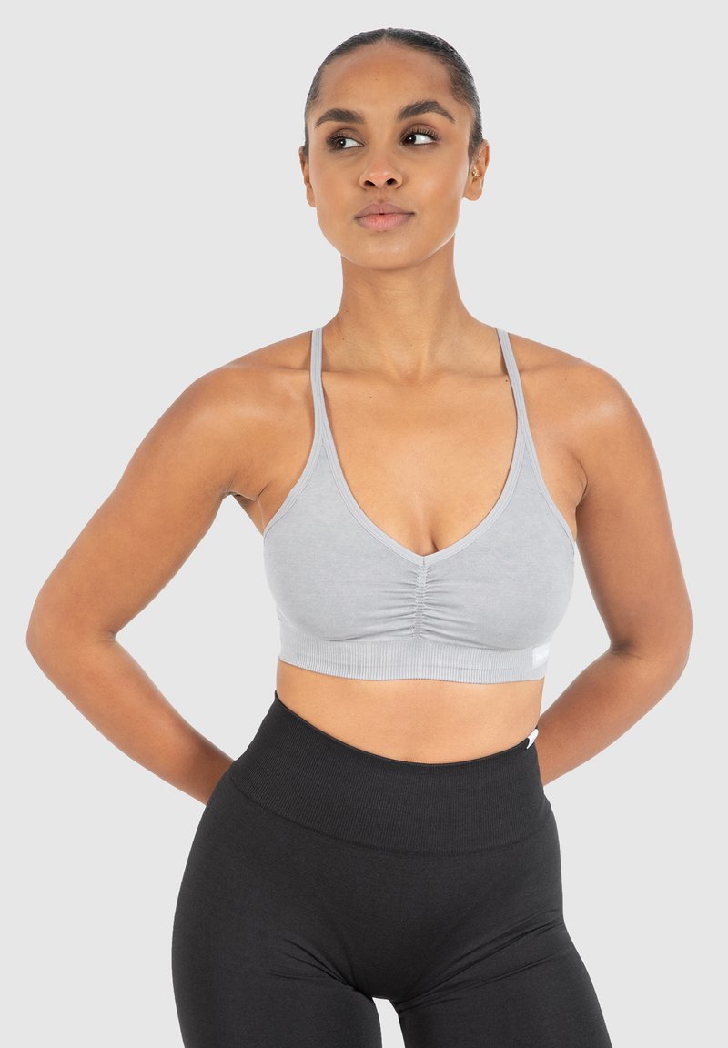 Grijze sportbra met een V-halsontwerp, gathered frontdetail, geribbeld zoom en dunne schouderbanden, gecombineerd met hoog-waist zwarte leggings.