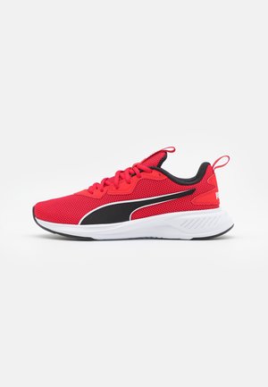 Czerwony sportowy sneaker z czarnym i białym logo Puma, białą podeszwą, siateczkową cholewką oraz pętelkami do zakładania na języku i pięcie.