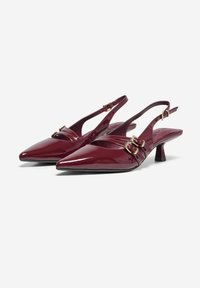Talons slingback vernis bordeaux avec des bouts pointus et un petit talon. Présente des doubles brides décoratives avec des accents en métal doré.