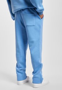 Hellblaue Sweatpants aus weichem Stoff, mit einer Gesäßtasche, gerippten Bündchen und einer lässigen Passform. Kombiniert mit weißen Sneakers.