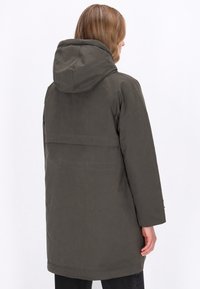 Mørkegrøn parka med hætte, der har en lang silhuet, glat tekstur og minimale syninger på bagsiden.