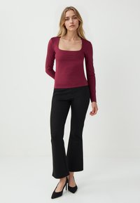 Top bordeaux a maniche lunghe con scollo quadrato, abbinato a pantaloni neri a palazzo e scarpe con tacco alto nere, su uno sfondo neutro.