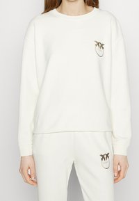 Biały sweatshirt z okrągłym dekoltem i długimi rękawami. Posiada mały, złoty detal logo na piersi. Miękki, gładki materiał.