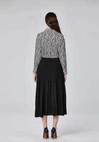 Jupe plissée noire avec une taille ajustée, accompagnée d'une blouse à col avec un motif floral noir et blanc. Des chaussures à talons complètent le look.