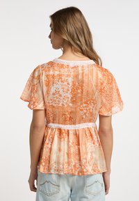 Top peplum in stampa paisley arancione e crema, tessuto trasparente, maniche a sbuffo corte, bordino in pizzo scallopato al collo e in vita.
