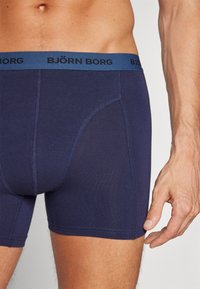 Tamnoplave bokserice izrađene od mekog materijala, s prilagođenim dizajnom, kontrastnim plavim pojasom s logotipom "BJÖRN BORG" i ravnim šavovima.