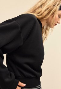 Schwarzer Pullover mit Rundhalsausschnitt, strukturierter Stoff und geripptem Saum. Verfügt über überschnittene Schultern und eng anliegende Bündchen.