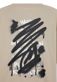 Maglietta a maniche corte beige con un design grafico in stile spray nero. Presenta un testo bianco audace parzialmente coperto da tratti neri.