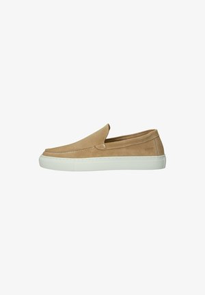 Zapatilla tipo slip-on de ante color beige con suela de goma blanca, diseño minimalista y detalles de costura a lo largo de los bordes.