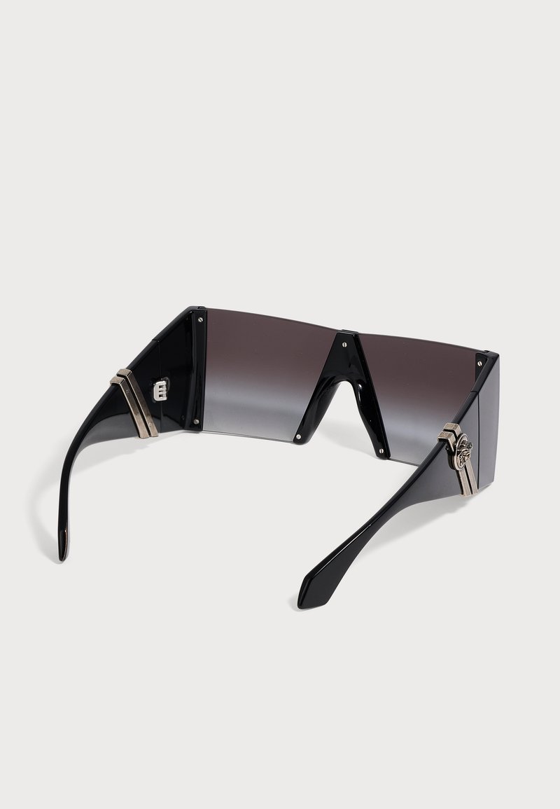 Lunettes de soleil futuristes enveloppantes noires avec une seule lentille teintée foncée et des accents décoratifs argentés sur les branches.