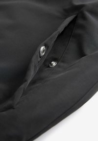Tessuto nero con una superficie liscia, dotato di chiusura a bottoni e una tasca interna, che offre un design pulito e funzionale.