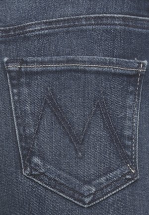 Il tessuto in denim blu scuro presenta una tasca posteriore con una patta triangolare e un motivo di cucitura a zigzag in contrasto.