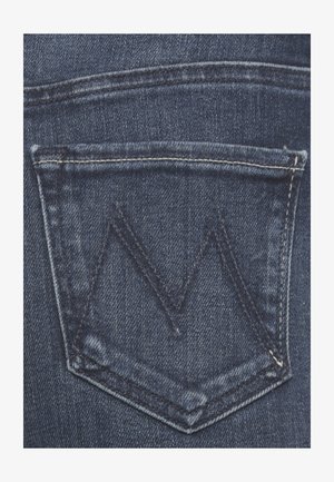 Il tessuto in denim blu scuro presenta una tasca posteriore con una patta triangolare e un motivo di cucitura a zigzag in contrasto.