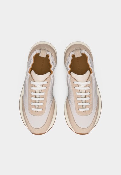 Ζευγάρι από μπεζ και λευκά καθημερινά αθλητικά παπούτσια με ελαστικό περιλαίμιο και λευκά κορδόνια, φωτογραφημένα από πάνω πάνω σε λευκό φόντο.