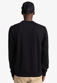 Sweat-shirt noir en coton avec col rond, poignets et taille côtelés. Vue de dos montrant un design minimaliste et une texture lisse.