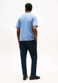 Maglietta in cotone blu con maniche corte, abbinata a pantaloni blu scuro. La maglietta ha un collo rotondo e un taglio dritto. Le scarpe sono mocassini neri.