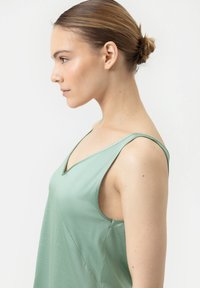 Een lichtgroene mouwloze top met een V-halsontwerp, een zachte textuur en subtiele stikdetails, nauwsluitend bij de schouders en vloeiend aan de onderkant.