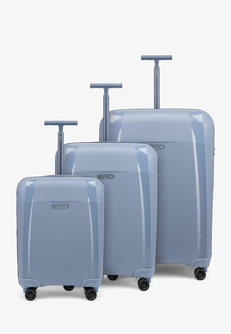 Trois valises rigides bleu clair de tailles différentes avec des poignées télescopiques étendues et quatre roues noires pivotantes chacune, alignées en rangée.