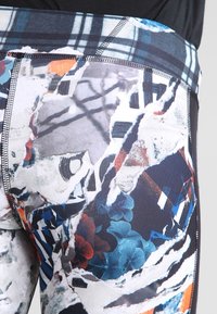 Acercamiento de leggings estampados con diseños abstractos de papel rasgado, flores y cuadros en colores negro, blanco, azul, rojo y naranja.