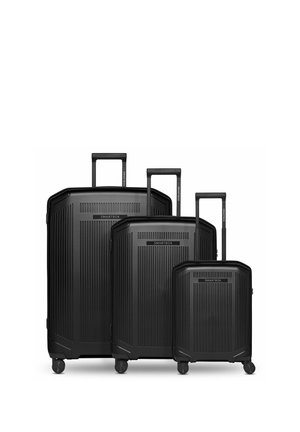 Tre valigie rigide nere di diverse dimensioni con maniglie telescopiche e quattro ruote, disposte affiancate su uno sfondo bianco.
