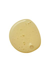 Beige crèmetextuur met een gladde, glanzende afwerking. Bevat kleine luchtbelletjes en heeft een ronde, onregelmatige vorm. Geplaatst op een witte achtergrond.