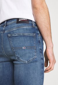 Modré džíny z denimu s přiléhavým střihem, na zadní straně s černou etiketou "TOMMY JEANS" a malým logem na pravé kapse.
