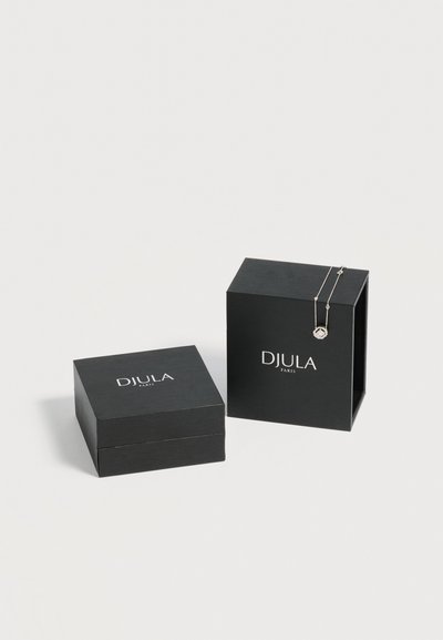 Deux boîtes à bijoux noires DJULA Paris, une fermée et une droite avec un collier pendentif en argent posé dessus.