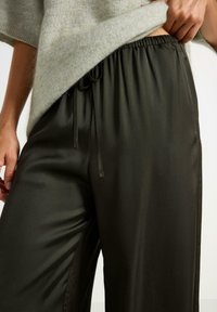 Pantaloni a gamba larga verde scuro realizzati in un materiale liscio, con vita elasticizzata e cordoncino, e tasche laterali.