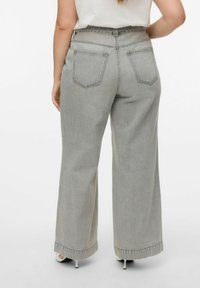 Jeans de pierna ancha en denim gris claro, con diseño de cinco bolsillos, dobladillo sin rematar y detalles de costura sutiles en los bolsillos traseros.