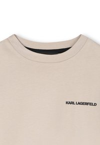 Beige katoenen T-shirt met een ronde halslijn en korte mouwen. Heeft een zwart "KARL LAGERFELD" logo op de linkerborst. Soepele textuur.