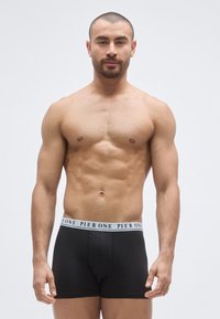 Μαύρα ανδρικά εσώρουχα μποξέρ με λευκή ελαστική μέση που φέρει το κείμενο «PIER ONE». Λείο ύφασμα, εφαρμοστή σχεδίαση, απλή και λειτουργική μορφή.