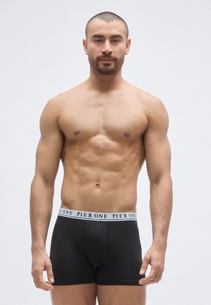 Boxer noir avec une ceinture élastique blanche portant le texte "PIER ONE". Tissu lisse, coupe ajustée, forme simple et fonctionnelle.