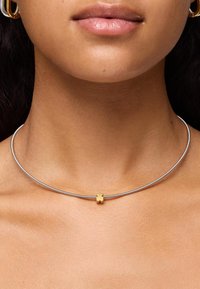 Collana choker in argento con un design liscio e arrotondato; presenta un piccolo accento a forma di fiore dorato al centro.