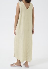 Robe longue à rayures jaune clair et crème. Présente un décolleté en V dans le dos, un style sans manches et des fentes latérales pour faciliter les mouvements.