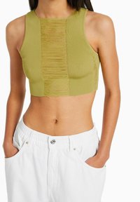 Zelený průhledný crop top s texturovaným středovým panelem, přiléhavý střih a kulatý výstřih. Nosený s bílými šortkami na elastický pas.