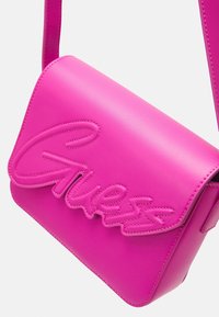 Borsa a spalla in pelle rosa con chiusura a patta magnetica, caratterizzata da un logo "Guess" in corsivo in rilievo. Texture liscia con dettagli di cucitura visibili.