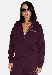 Bordowa bluza z kapturem na zamek błyskawiczny, z kieszeniami z przodu, z białym haftem logo. Miękka, teksturowana tkanina z kapturem ze sznureczkiem i ściągaczami na mankietach.
