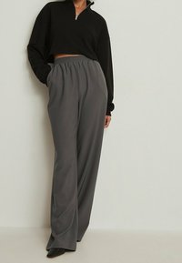 Schwarzer, kurzer Zip-Halspullover mit Mock-Neck, kombiniert mit weit geschnittenen grauen Hosen mit elastischem Bund und glattem Stoff.