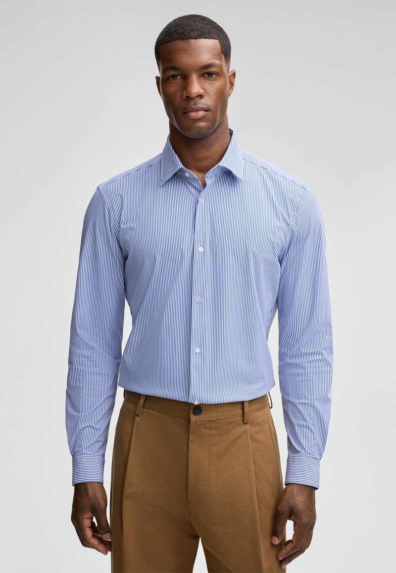 Camicia a righe blu chiaro e bianca con colletto classico, maniche lunghe e design aderente, abbinata a chinos color sabbia.